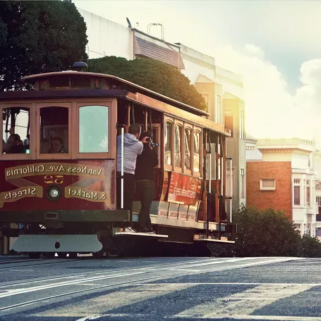 Un tranvía rodea una colina en San Francisco con pasajeros mirando por la ventana.